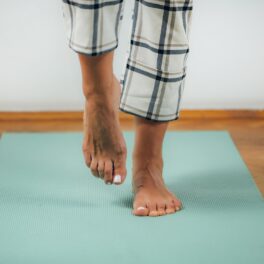 Persoană care poartă o pijama alb cu negru, care stă într-un picior pe un covor albastru, pe o podea din lemn, pentru a ilustra statul într-un picior timp de 10 secunde