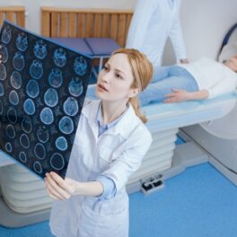 Doctoriță care se uită la un RMN cu creier, cu o pacientă în spate în RMN, pentru a ilustra una dintre cauzele bolii Alzheimer