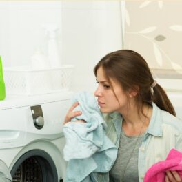 Femeie brunetă care scoate hainele din mașina de spălat și le miroase, ca femeia care poate mirosi boala Parkinson