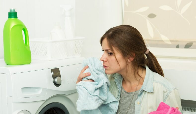 Femeie brunetă care scoate hainele din mașina de spălat și le miroase, ca femeia care poate mirosi boala Parkinson