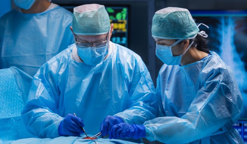 2 chirurgi îmbrăcați în halate albastre, care operează, pentru a ilustra cum o femeie și-a donat uterul pentru sora sa