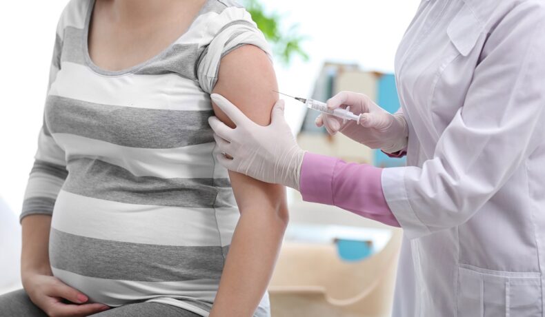 Femeie însărcinată îmbrăcată în bluză cu dungi albe și gri, care primește un vaccin de la o doctoriță, pentru a ilustra cum a fost autorizat un nou vaccin pentru femeile însărcinate