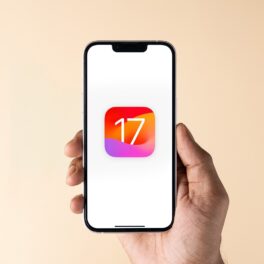 Utilizator care ține un telefon în mână, cu logo-ul iOS 17 pe ecran, pe fundal galben, acum că Apple lansează iOS 17