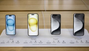 Cele 4 modele din seria iPhone 15, expuse pe un fundal de lemn deschis la culoare și un suport alb, lansate pe 12 septembrie 2023, pentru a ilustra cum să verifici dacă ai cumpărat un iPhone 15 nou original