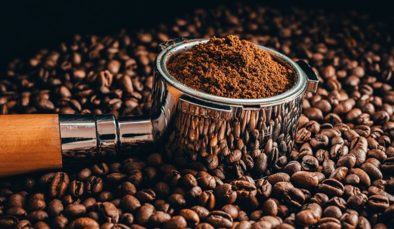 Boabe de cafea împrăștiate, cu un recipient în care se află zaț de cafea, deasupra lor, pentru a ilustra cum experții pot folosi zațul de cafea