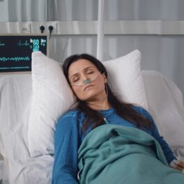 Femeie brunetă care e într-un pat de spital, bolnavă, similară cu pacienta care a fost infectată cu bacteria mortală