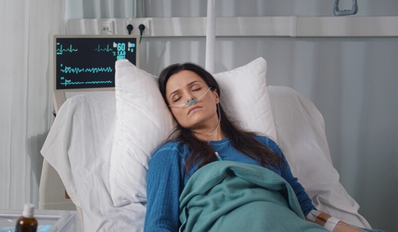 Femeie brunetă care e într-un pat de spital, bolnavă, similară cu pacienta care a fost infectată cu bacteria mortală