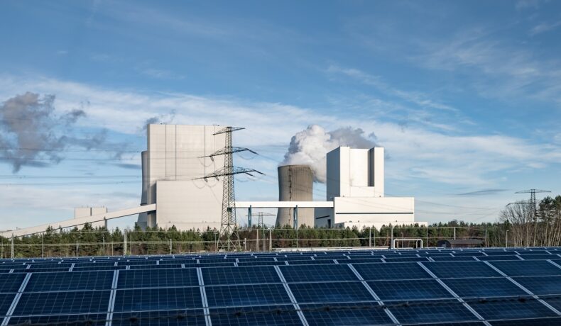 Panouri solare, pe fundal o centrală energetică, pentru a ilustra cea mai importantă sursă energetică