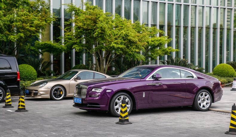 O mașina Rolls Royce mov, e stradă, lângă un Porsche auriu