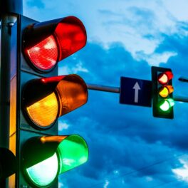 Semafoare pe stradă, cu fundalul pe cer, culoarea verde aprinsă, pentru a ilustra de ce au semafoarele culorile roșu, galben și verde
