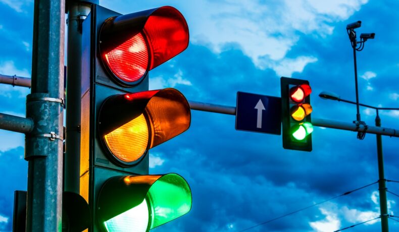 Semafoare pe stradă, cu fundalul pe cer, culoarea verde aprinsă, pentru a ilustra de ce au semafoarele culorile roșu, galben și verde