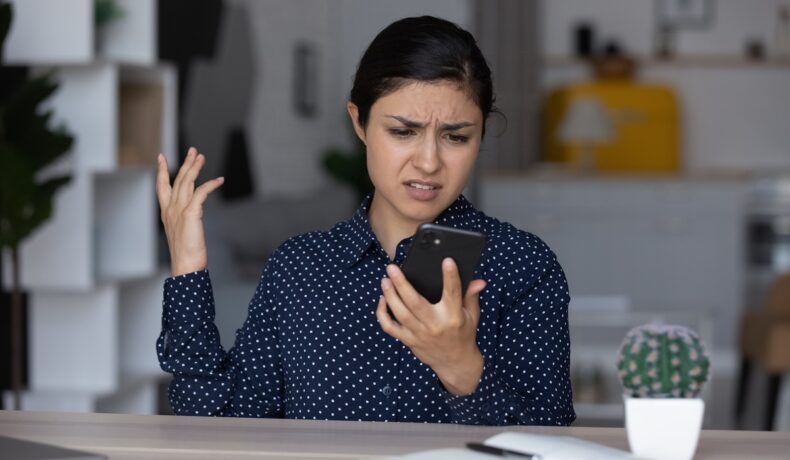 Femeie care stă la birou și se uită la telefon, îmbrăcată în bluză albastră, pentru a ilustra de ce sună toate telefoanele din SUA la aceeași oră