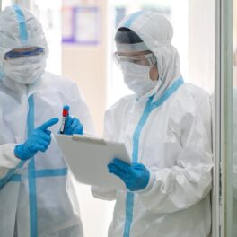 Doctori îmbrăcați în combinezoane albe, care studiază o mostră, ca experții care au de-a face cu o nouă epidemie care se răspândește în Asia