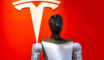 Robot Optimus, care stă în fața unui logo Tesla roșu, pentru a ilustra cum Tesla a dezvăluit Optimus Gen 2