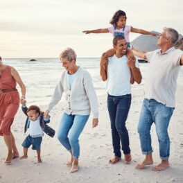 Familie cu 3 generații pe plajă, zâmbind și distrându-se, pentru a ilustra cum familiile nu vor mai fi la fel pe viitor