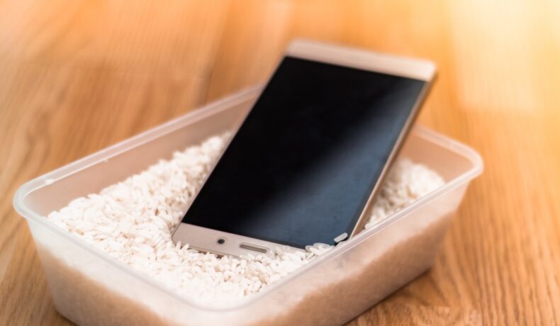 Telefonul în orez, o metodă să îl usuci care nu e recomandată de experți, într-un recipient transparent, pe fundal de lemn