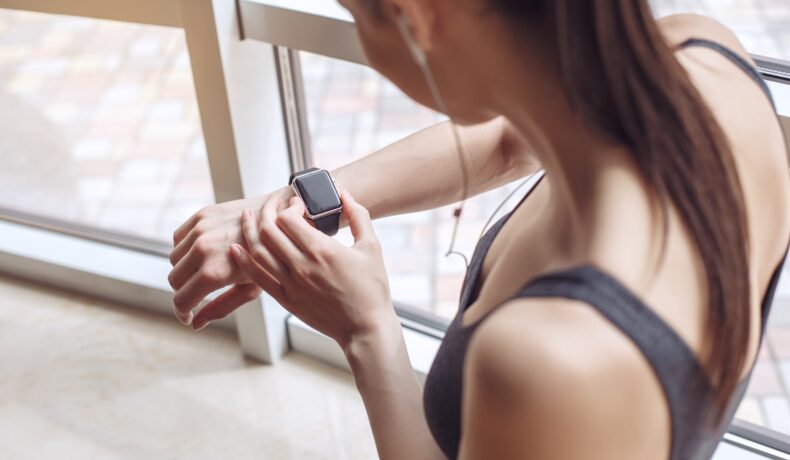 Femeie îmbrăcată sport care își verifică ceasul de la mână, pentru a ilustra cum timpul e cu 9% mai lent pentru oameni la sală